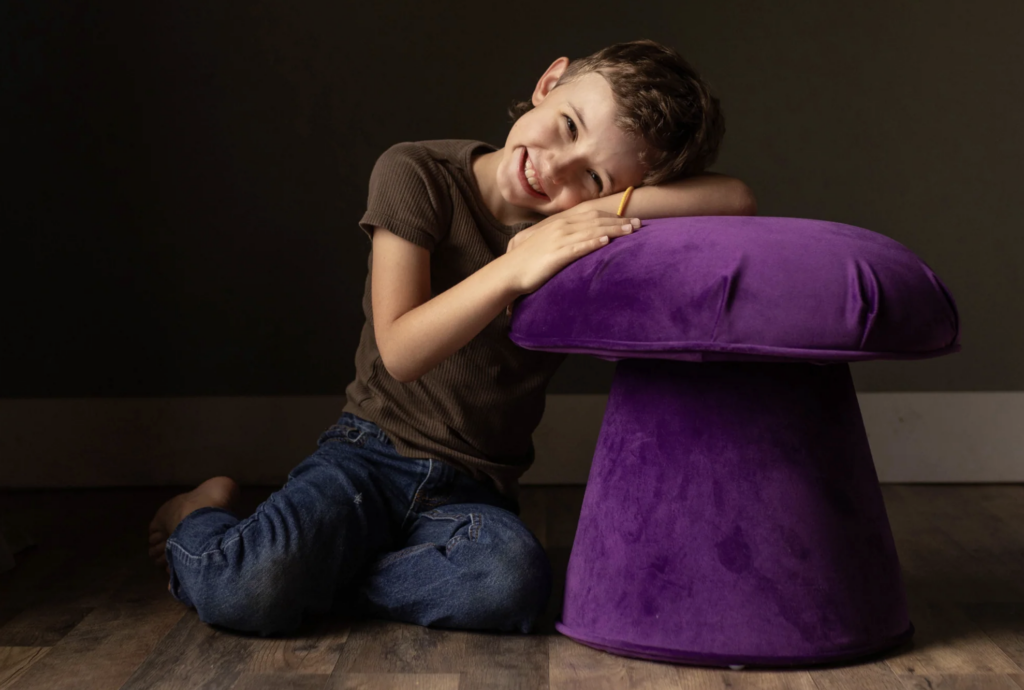 A boy resting his head on a Velvet Mushroom Stool in Plum